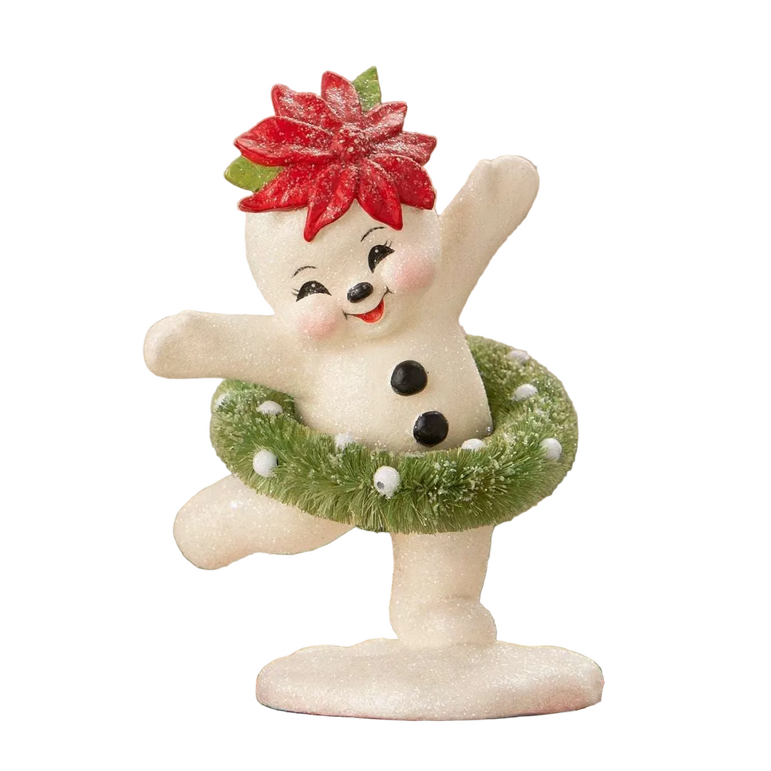 A festive white snowman figurine dancing with one arm raised, wearing a red poinsettia on its head and a green wreath around its waist, displayed on a red box with a blurred holiday background.