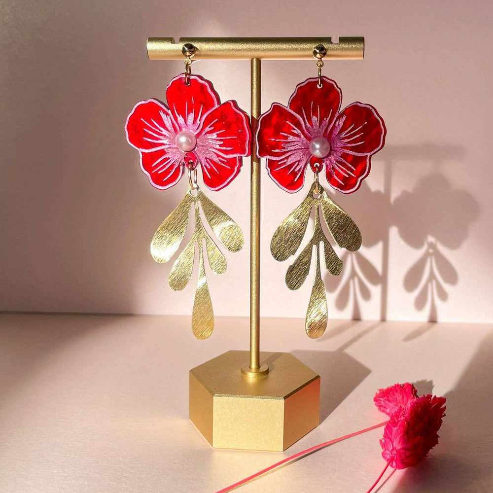 Red floral earrings on a gold stand with a pink flower on a light background