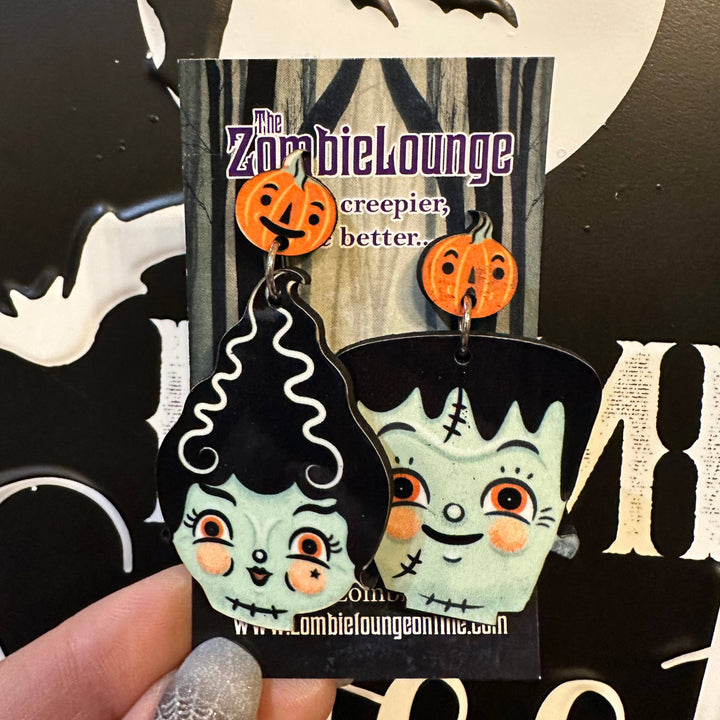 Halloween-themed earrings with a 'Zombie Lounge' label on a decorative background.