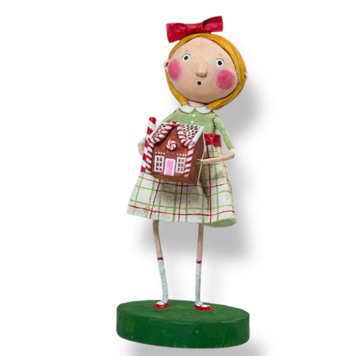 A Christmas figurine of a girl wearing a green and red plaid dress and holding a red and white house-shaped item, with a red bow in her hair, on a green base.