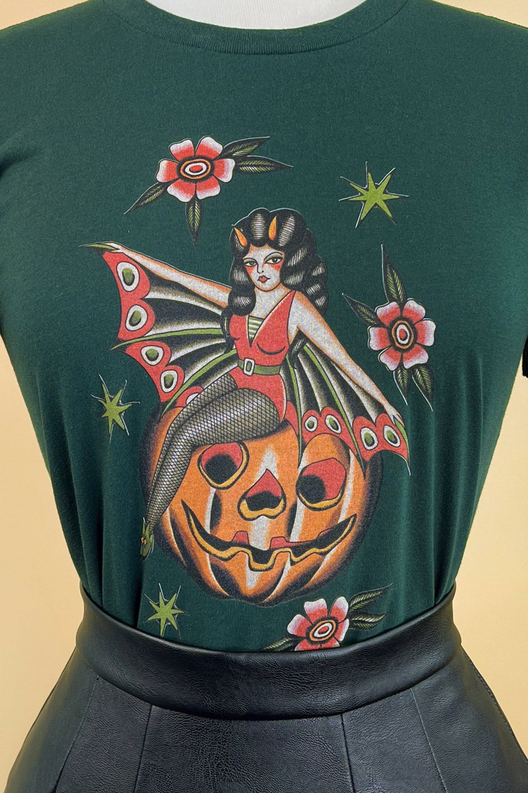 A person wearing a forest green t-shirt with a graphic print of a pumpkin and flowers.