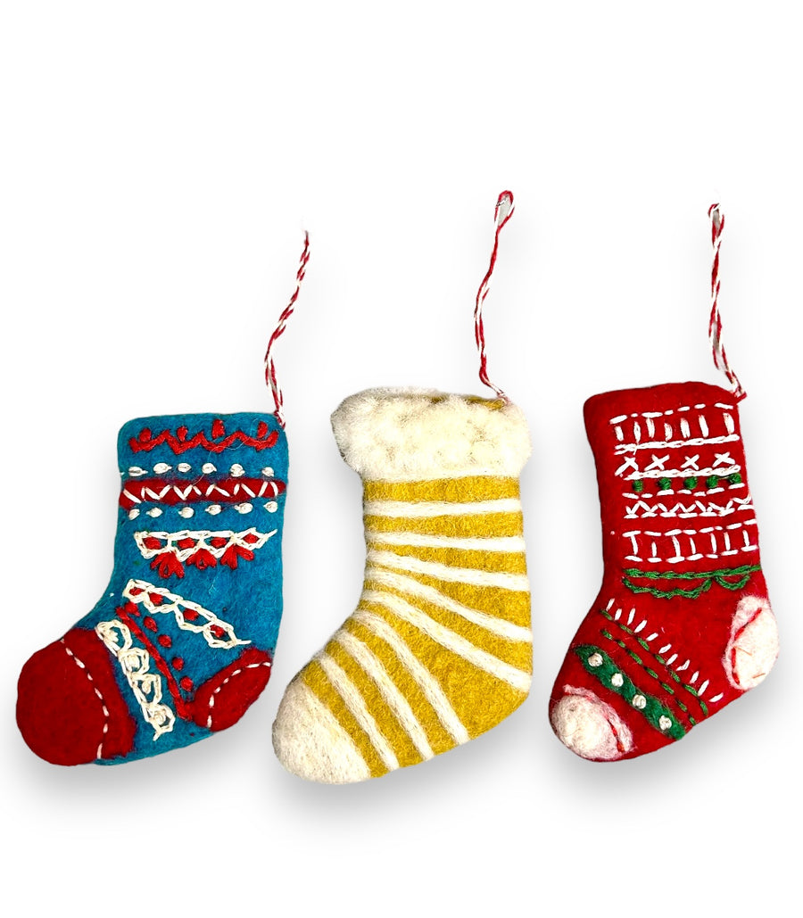A set of three felted wool Christmas stocking ornaments with embroidered designs, including a red and white stocking with a white cuff, a blue and yellow stocking with a yellow cuff, and a green and red stocking with a red cuff. Each ornament has a hanging ribbon and is against a white background.