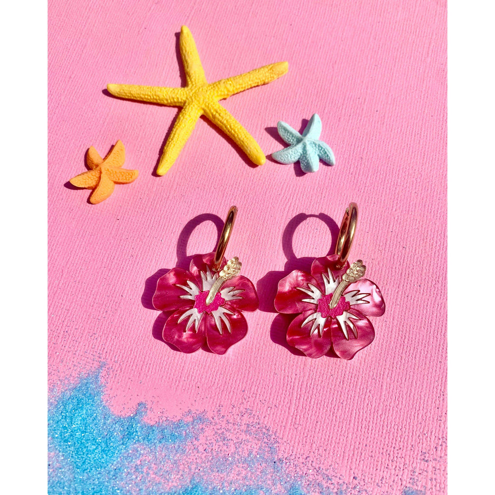 Pink flower-shaped earrings with gold hooks on a pink background with starfish decorations.