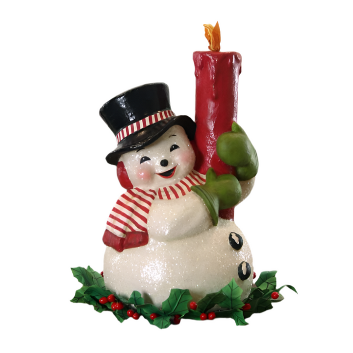 Bethany Lowe Christms decorative figurine of a snowman holding a red candle, adorned with a black top hat, red and white striped scarf, green gloves, and red earmuffs, set against a artificial holly and berries backdrop.
