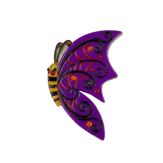 johanna_parker_batilda_butterfly_brooch_lipstick_and_chrome A purple bat-wing shaped brooch with black scrollwork, small orange gem accents, and a yellow-and-black striped bee body on a plain white background.