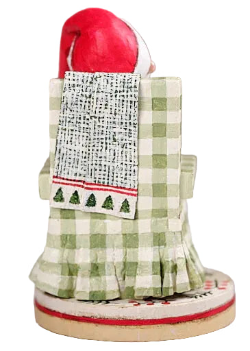 Decorative figure of a person wearing a green checkered dress with a red hat and white apron on a gray background.