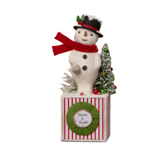 A festive snowman figurine with a black top hat and red scarf standing on a striped base with a 'Merry and Bright' medallion.