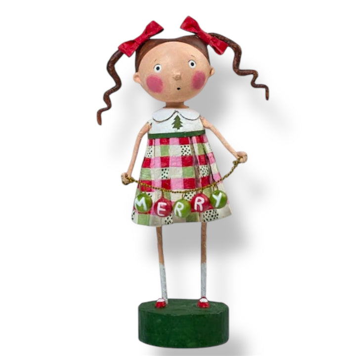 A Christmas figurine of a girl wearing a red and green plaid dress with the text 'MERRY' on it, standing on a green base.