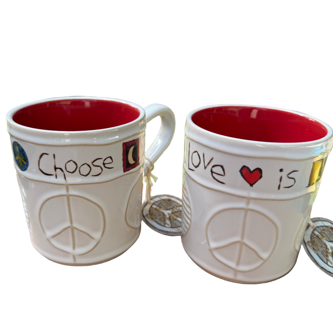 Two white mugs with red interior, peace symbol, and text on a wooden surface with a grassy background.