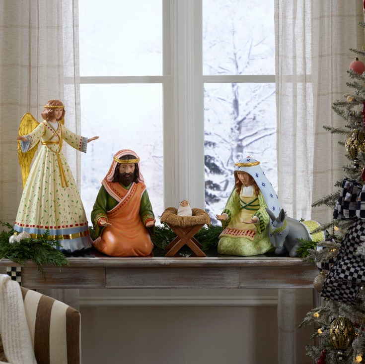 Nativity scene on a fireplace mantle with a decorated Christmas tree in the background.