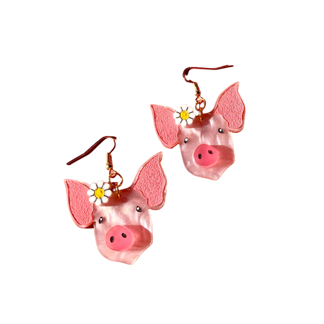 Pink pig-shaped earrings on a pink background with disco balls.