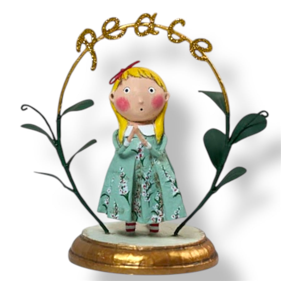 A Christmas figurine featuring a stylized character with blonde hair, wearing a green dress with a floral pattern, praying with the word 'PEACE' above her head, set against a white background.