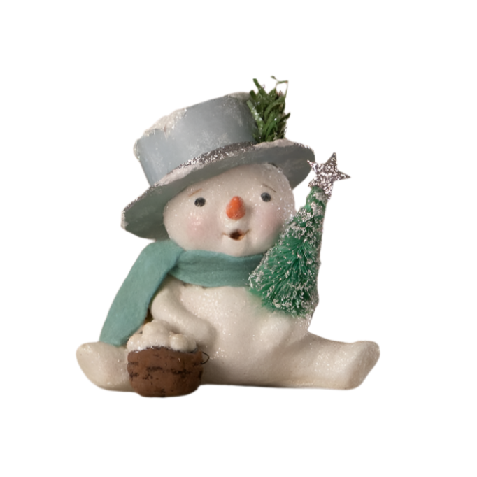 A seated snowman figurine wearing a soft aqua blue top hat with a snowflake-printed paper, holding a festive bottle brush tree.
